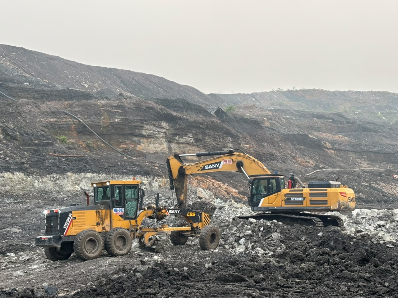 Excavator dan motor grader di area tambang terbuka