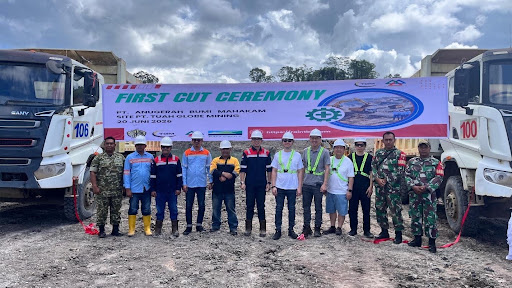 Tim kontraktor berfoto di depan spanduk first cut ceremony dan dua dump truck