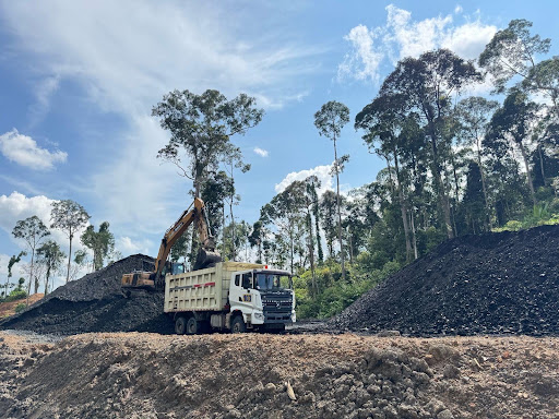 Excavator dan dump truck di antara timbunan material