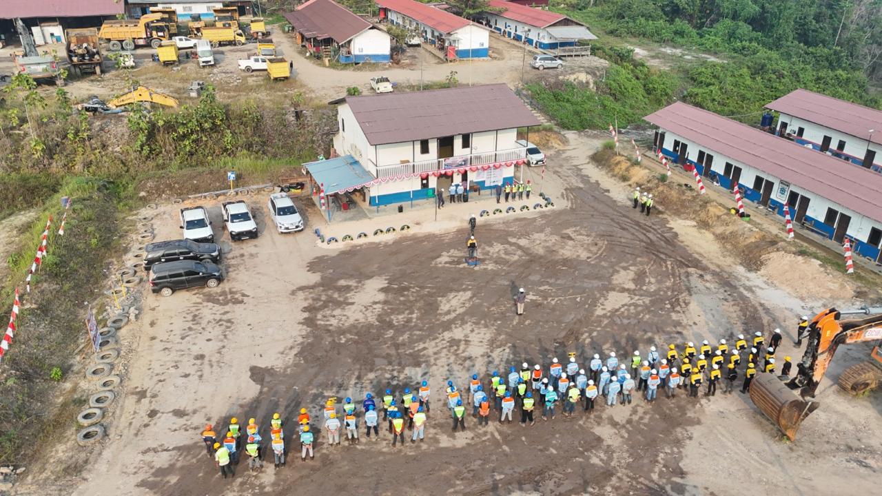 Foto udara pekerja dengan helm dan rompi keselamatan berbaris dalam apel K3 di depan kantor lapangan